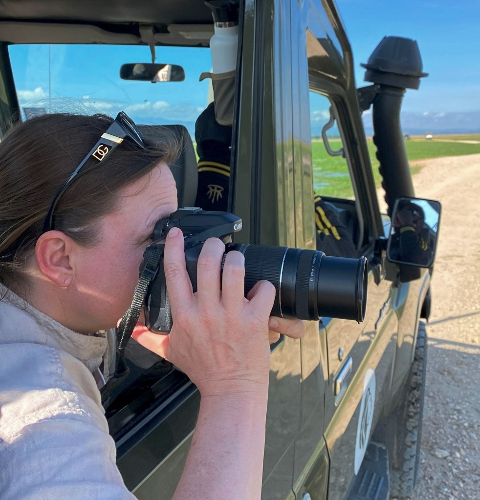 Adele Heidenreich leaning out of a safari vehicle, taking photos with a camera