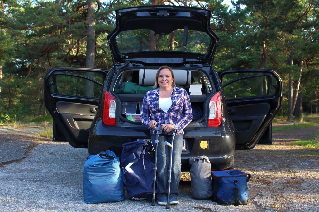 Adele Heidenreich standing with crutches beside an open car boot packed for a road trip