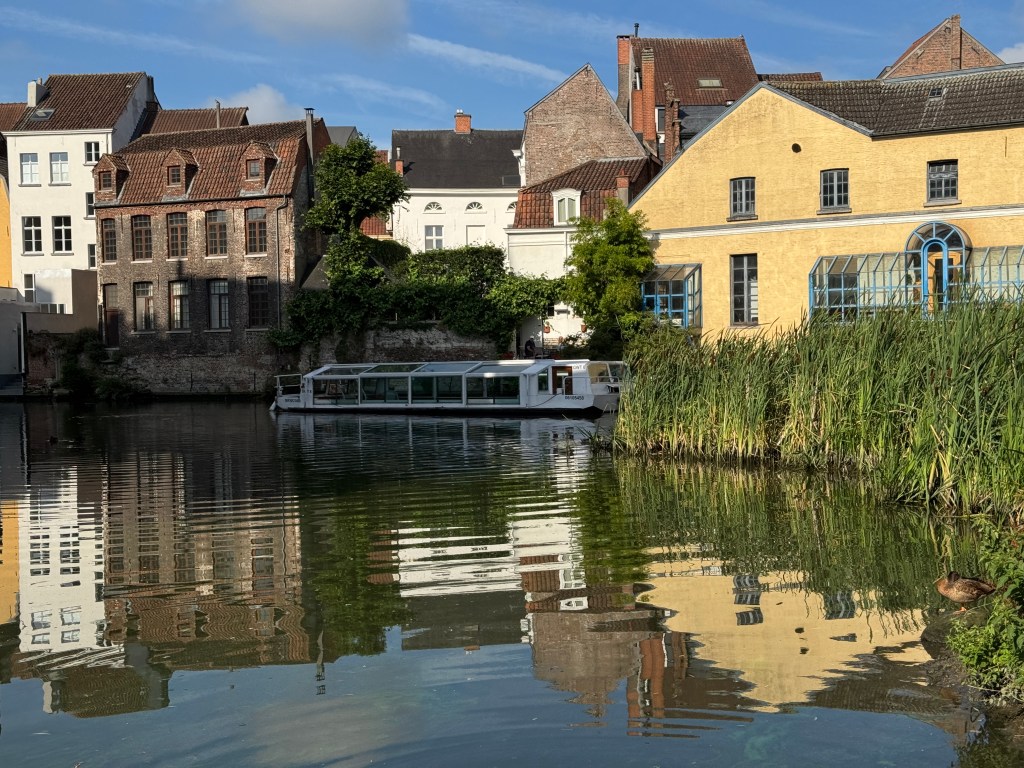 Canal in Ghent with historic buildings, a sightseeing boat, and reflections in the water