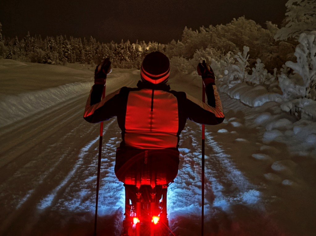 Skier in an adaptive sit-ski with red brake lights at night